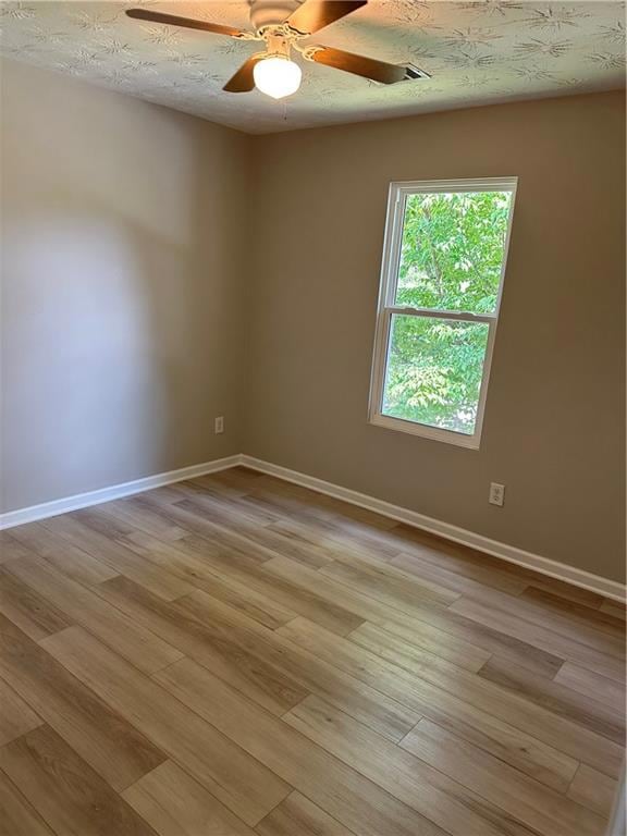 Empty room featuring a textured ceiling, light wood-style floors, and a ceiling fan