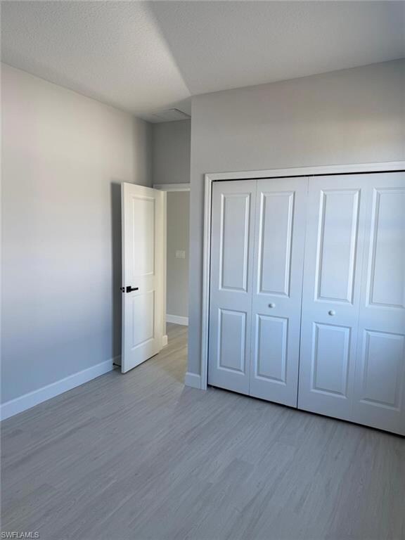 Unfurnished bedroom featuring wood finished floors, baseboards, and a closet