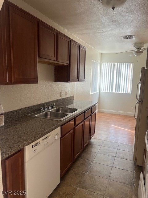 Kitchen featuring visible vents, dishwasher, dark countertops, a textured ceiling, and a sink