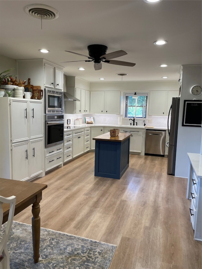 Kitchen featuring white cabinets, island, light wood-style floors, dishwasher, oven, and fridge
