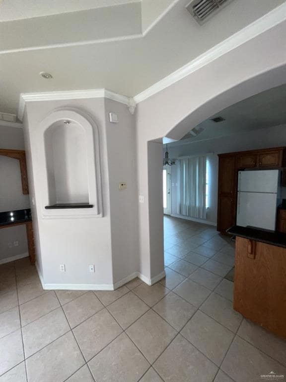 Empty room with light tile patterned flooring, crown molding, and arched walkways
