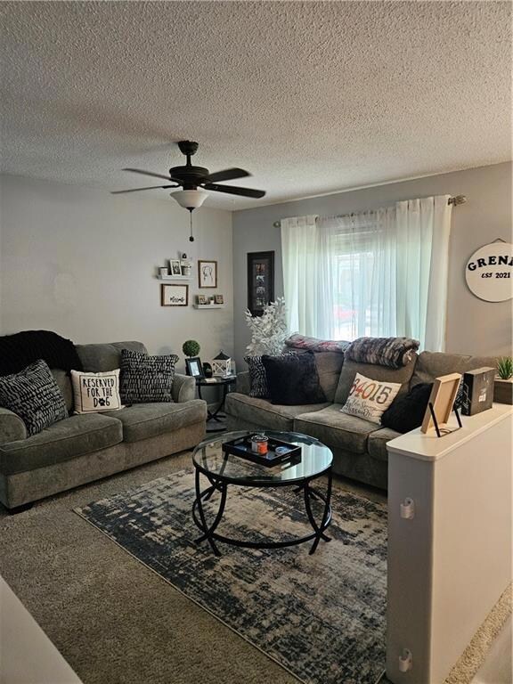 Carpeted living room with ceiling fan and a textured ceiling