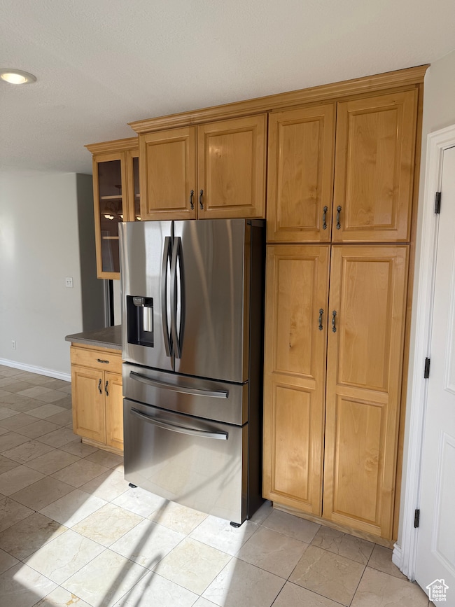 Kitchen featuring stainless steel fridge, light tile patterned flooring, glass insert cabinets, and dark countertops