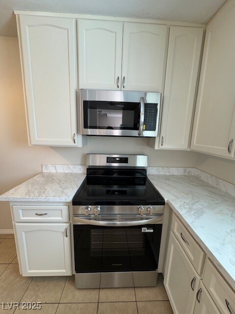 Kitchen with stainless steel appliances, light tile patterned flooring, and white cabinets