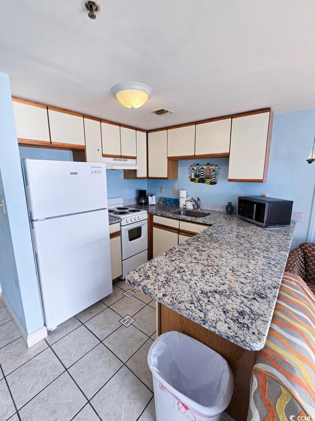Kitchen with white appliances, a peninsula, under cabinet range hood, a sink, and white cabinets