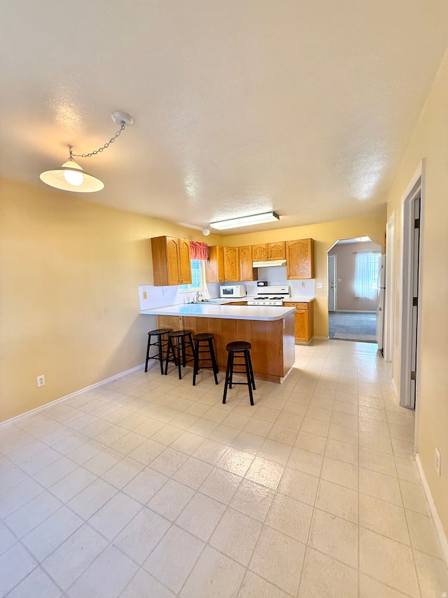 Kitchen featuring light countertops, a kitchen breakfast bar, arched walkways, brown cabinetry, and a peninsula