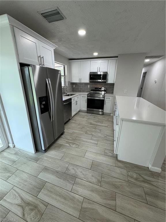 Kitchen featuring stainless steel appliances, white cabinets, wood finish floors, decorative backsplash, and a textured ceiling
