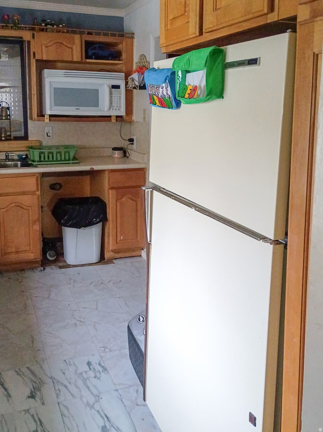 Kitchen featuring white appliances, light countertops, light marble finish flooring, brown cabinets, and crown molding