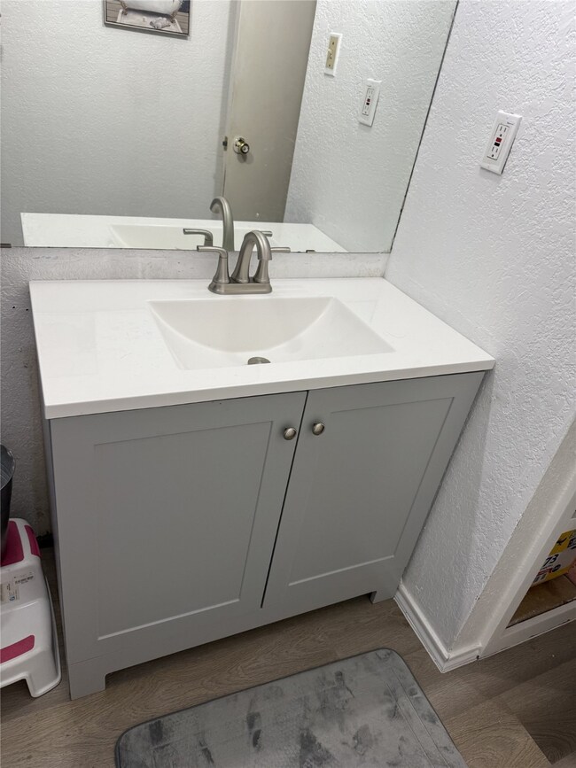 610A - Bathroom featuring a textured wall, NEW vanity and Light-wood style luxury plank flooring.