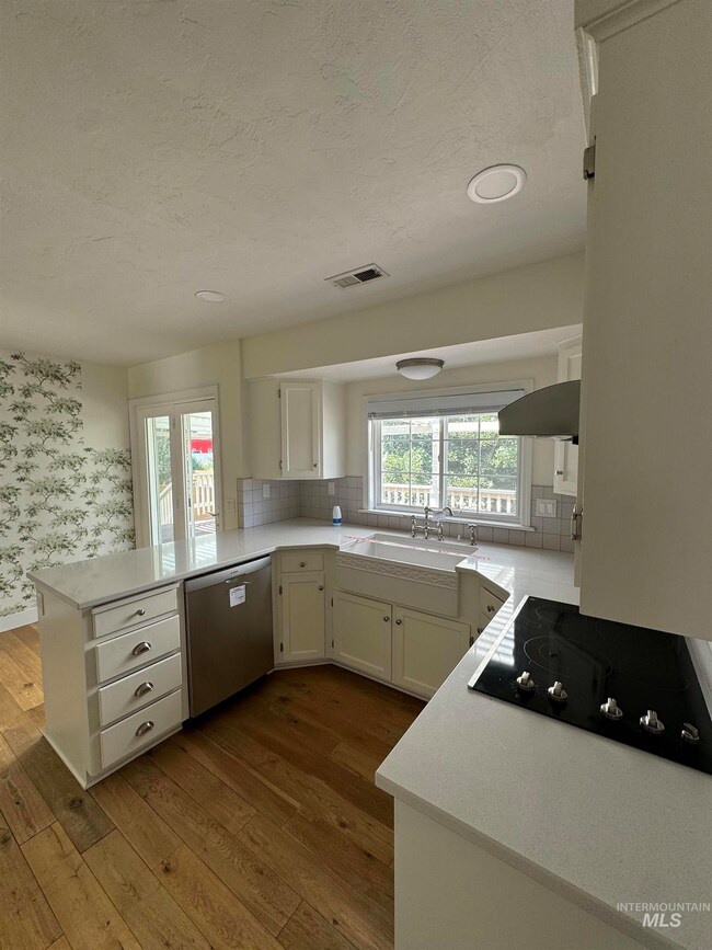 Kitchen with stainless steel dishwasher, black electric cooktop, a peninsula, dark wood-style floors, and a textured ceiling
