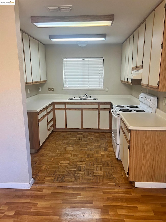 Kitchen with white electric range oven, light countertops, under cabinet range hood, and dark wood-type flooring