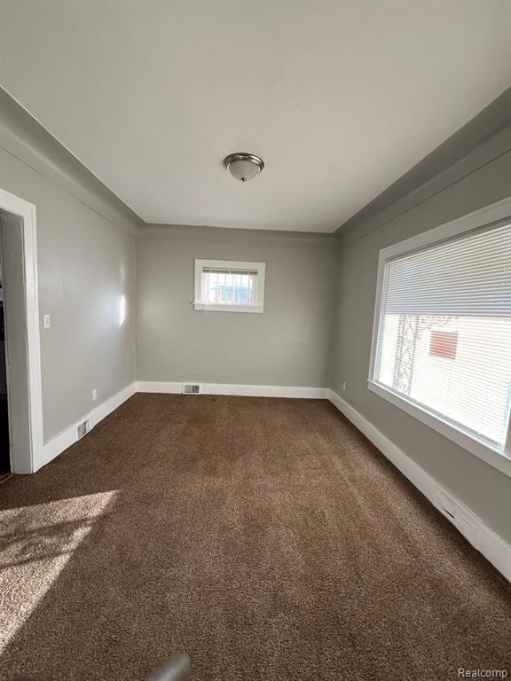 Unfurnished room featuring dark colored carpet and baseboards