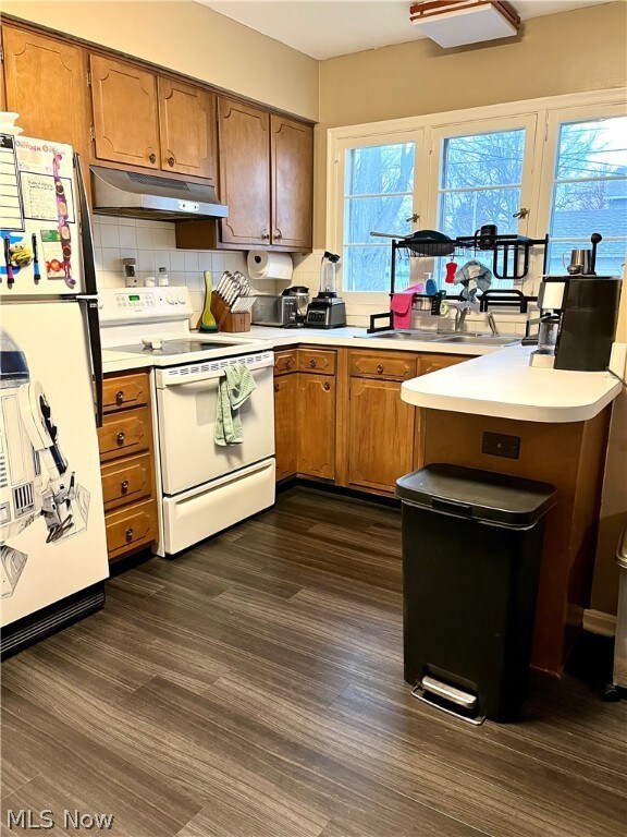 Kitchen with kitchen peninsula, tasteful backsplash, dark wood-type flooring, white appliances, and sink