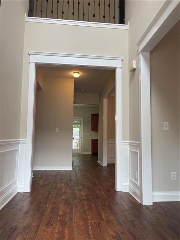Hallway featuring dark wood finished floors, wainscoting, and a decorative wall