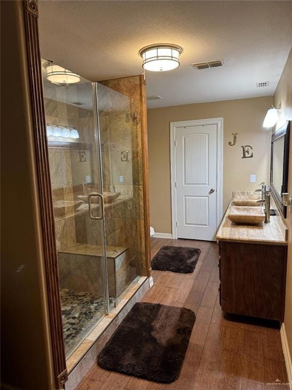 Bathroom featuring wood finished floors, double vanity, a stall shower, baseboards, and a textured ceiling