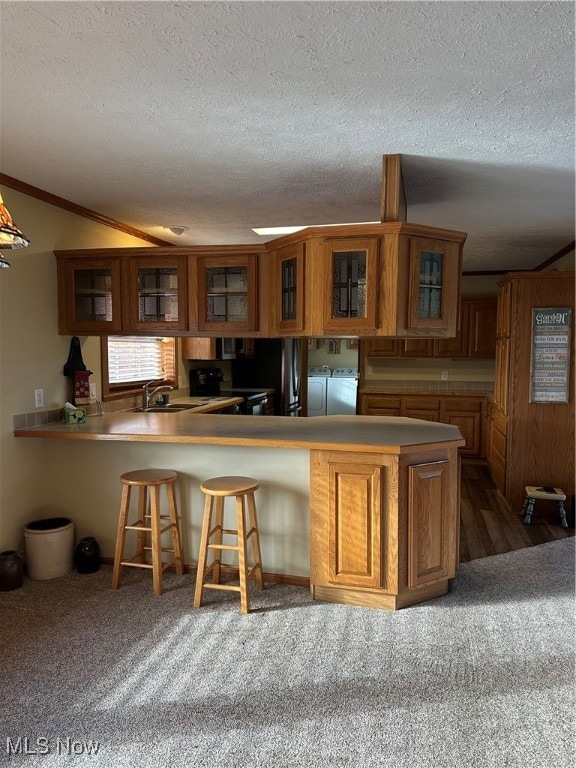 Kitchen with glass insert cabinets, a peninsula, a breakfast bar, brown cabinetry, and a textured ceiling