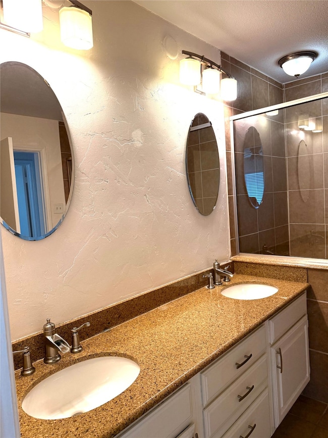 Bathroom featuring double vanity, a textured ceiling, a textured wall, and a tile shower