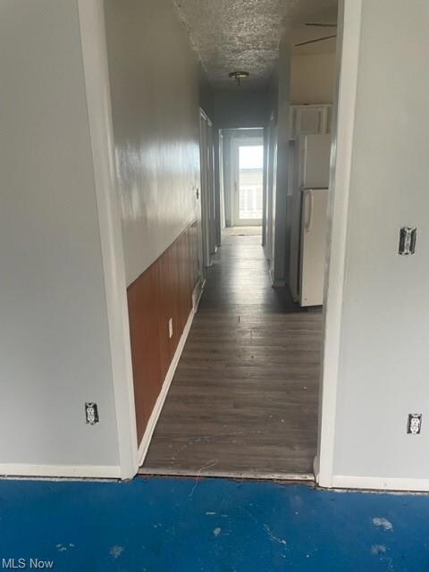 Hall with dark hardwood flooring and a textured ce
