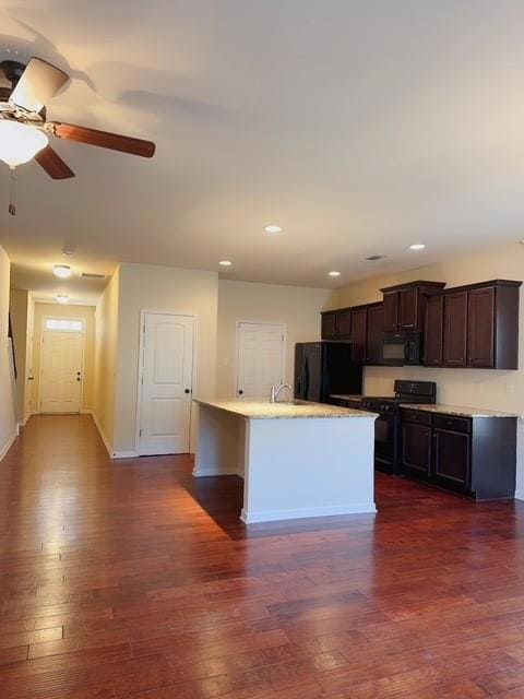 Kitchen with black appliances, dark wood finished floors, an island with sink, dark brown cabinetry, and recessed lighting