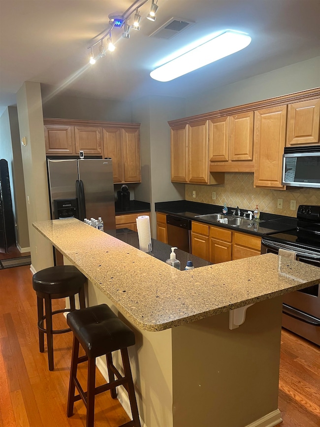 Kitchen with appliances with stainless steel finishes, a sink, hardwood / wood-style floors, and a breakfast bar