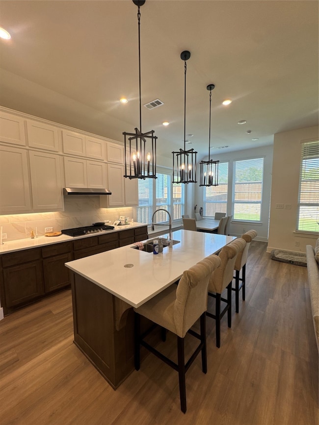 Kitchen featuring white cabinets, a breakfast bar, tasteful backsplash, dark wood finished floors, and an island with sink