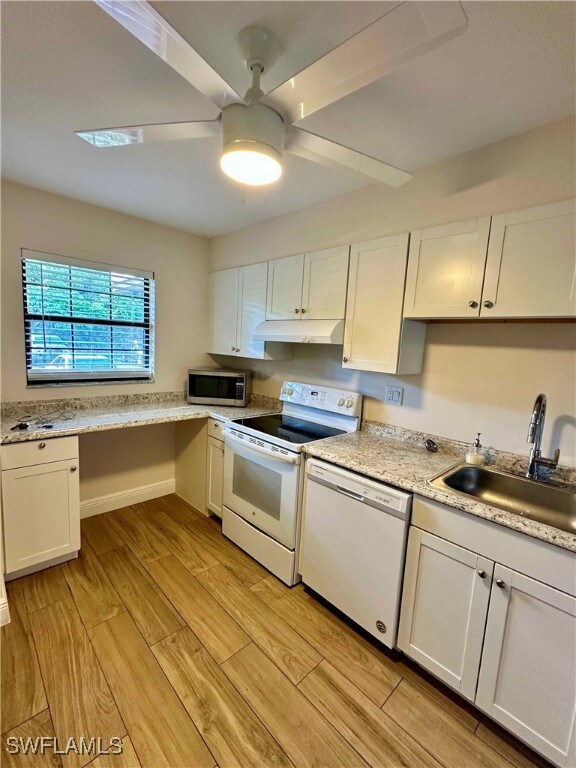 Kitchen with white appliances, white cabinets, light wood-type flooring, and under cabinet range hood