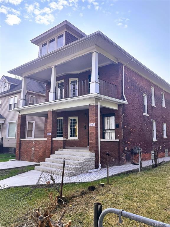 View of front of property featuring brick siding, a balcony, covered porch, and a front yard