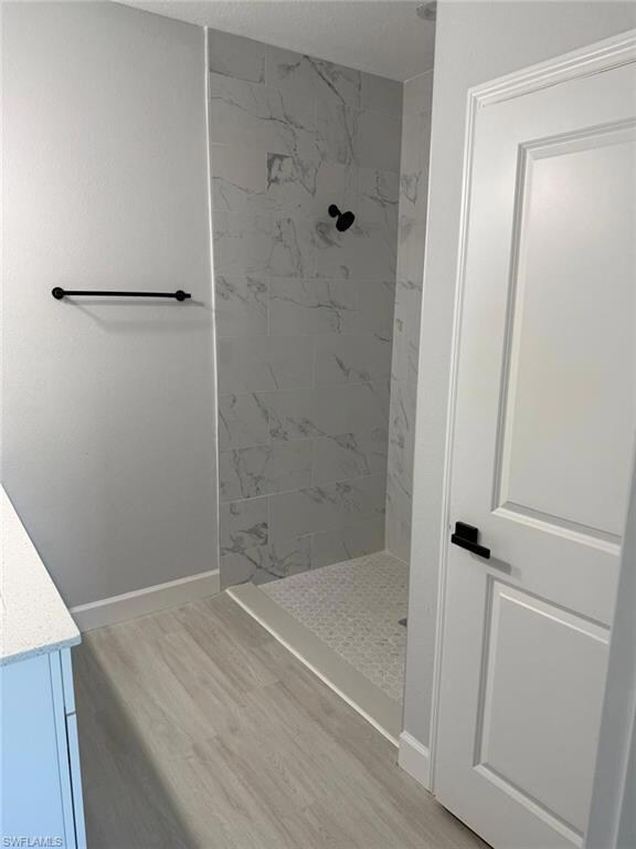Full bathroom with tiled shower, wood finished floors, baseboards, and vanity