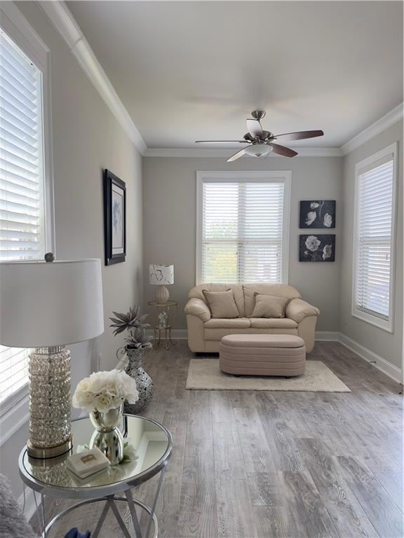 Living room with healthy amount of natural light, ornamental molding, wood finished floors, and a ceiling fan