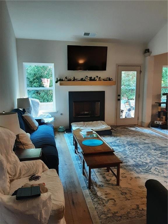 Living room with a fireplace, wood-type flooring, and vaulted ceiling
