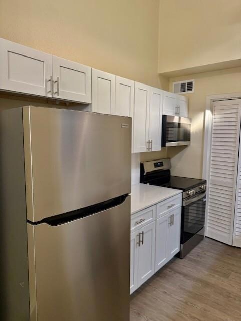 Kitchen with appliances with stainless steel finishes, white cabinetry, light wood finished floors, and light stone countertops