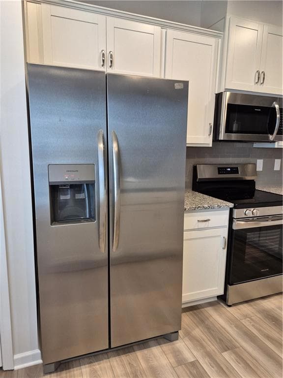 Kitchen with stainless steel appliances, white cabinets, light wood finished floors, and light stone counters