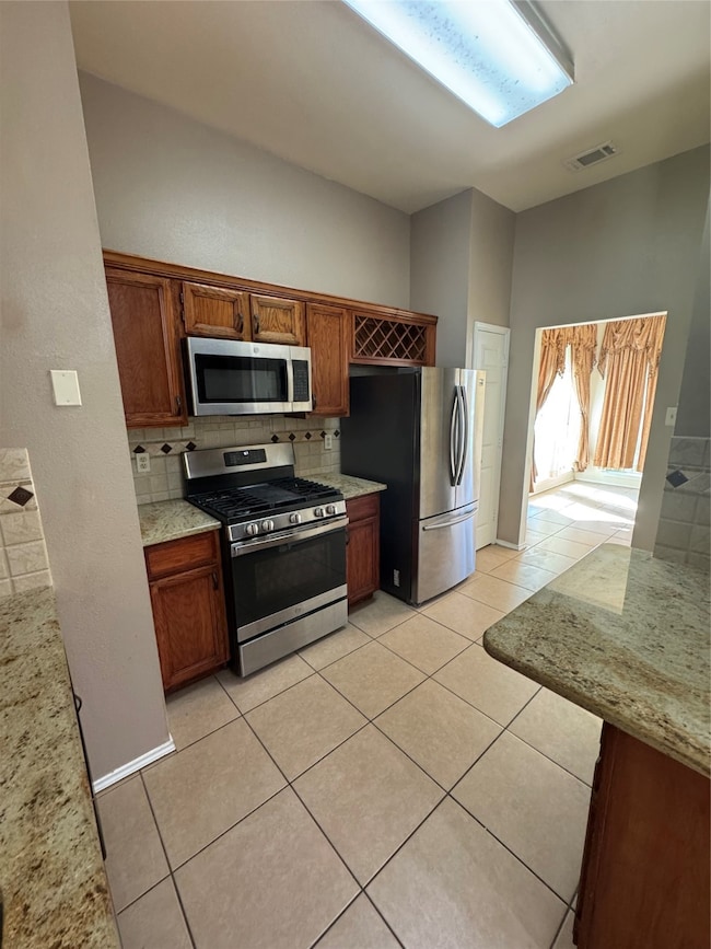 Kitchen with decorative backsplash, stainless steel appliances, and light stone counters