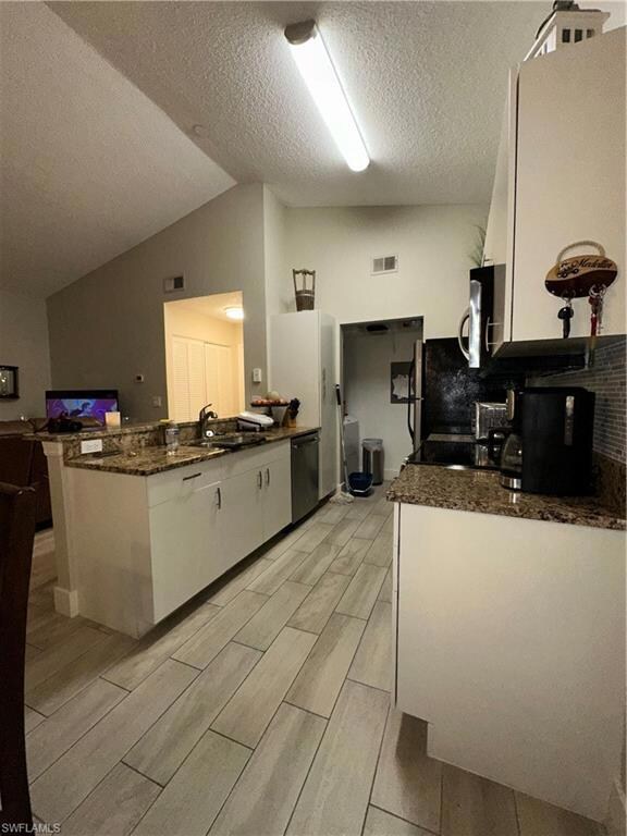 Kitchen featuring white cabinetry, vaulted ceiling