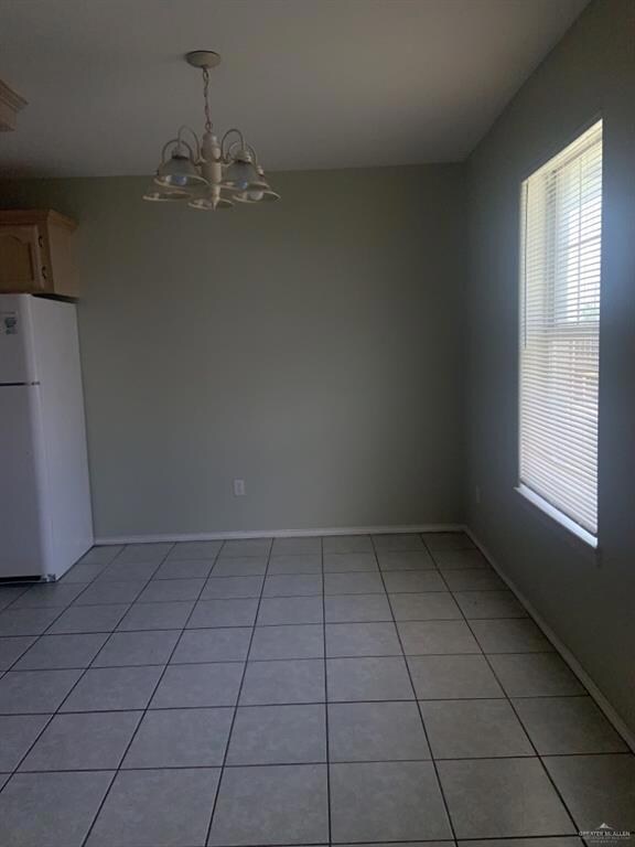 Unfurnished dining area with healthy amount of natural light, a chandelier, light tile patterned flooring, and baseboards