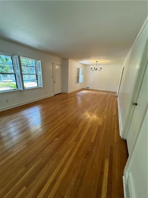 Unfurnished room featuring hardwood / wood-style floors, a notable chandelier, and ornamental molding