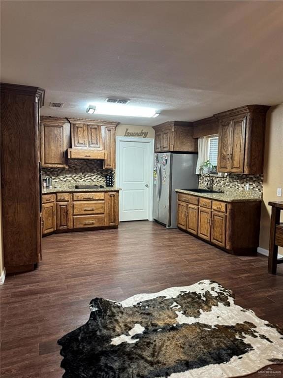 Kitchen featuring freestanding refrigerator, decorative backsplash, a sink, and under cabinet range hood
