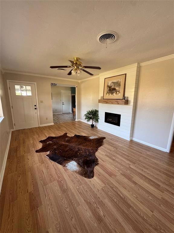 Living area featuring a large fireplace, ornamental molding, light wood-style floors, a ceiling fan, and a textured ceiling