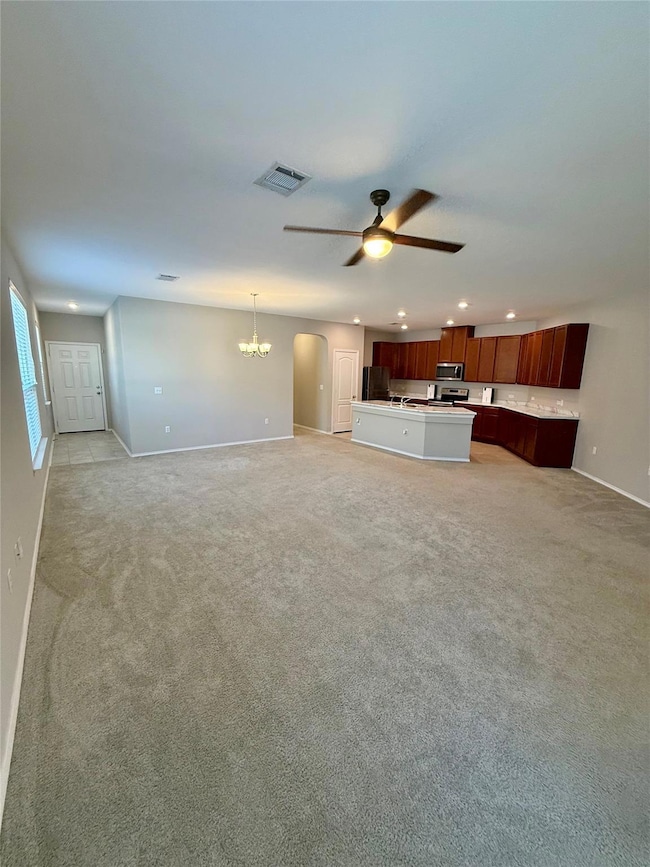 Unfurnished living room with arched walkways, a chandelier, light carpet, recessed lighting, and ceiling fan