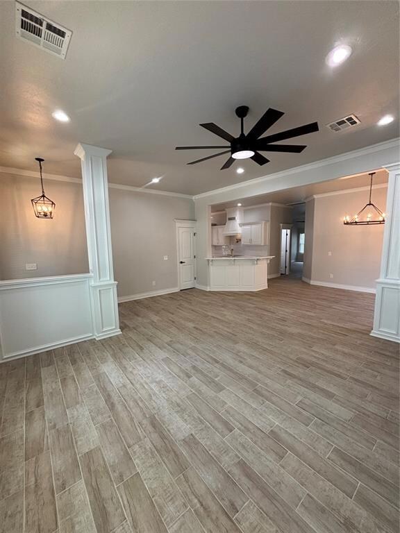 Unfurnished living room with ornamental molding, a ceiling fan, light wood finished floors, a chandelier, and recessed lighting