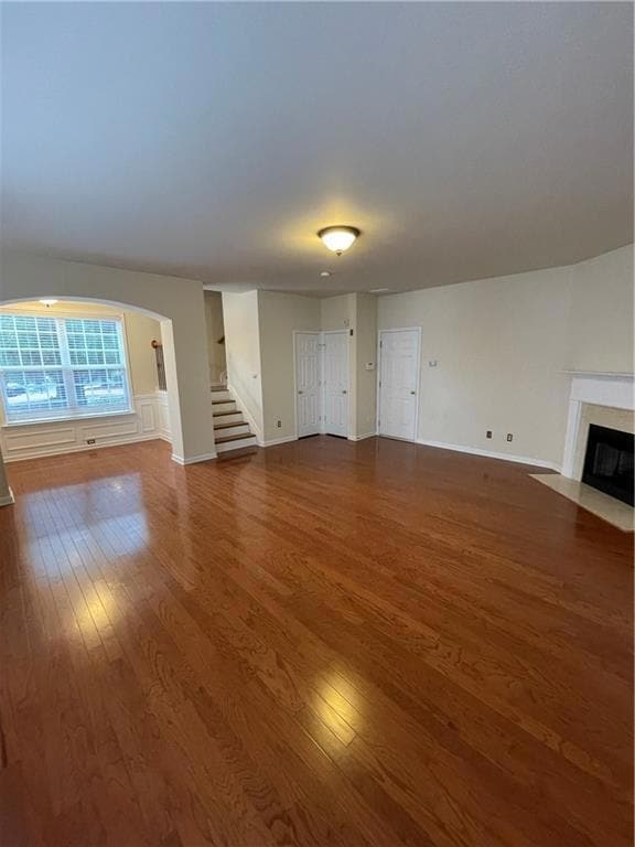 Unfurnished living room featuring stairway, dark wood finished floors, a premium fireplace, and baseboards