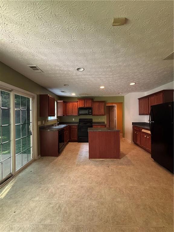 Kitchen featuring dark countertops, black appliances, a kitchen island, a textured ceiling, and dark brown cabinets