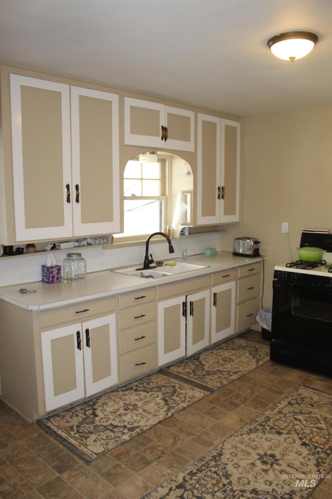 Kitchen featuring black gas stove, stone finish flooring, white cabinets, light countertops, and arched walkways