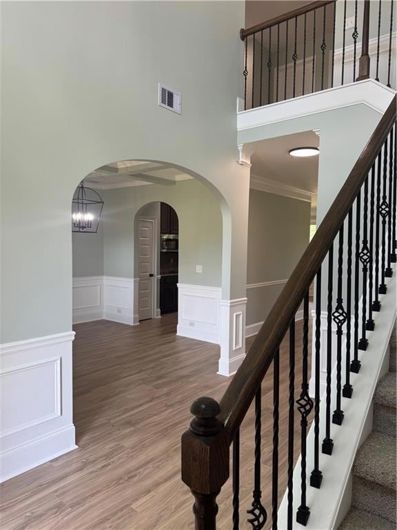 Staircase featuring a decorative wall, a high ceiling, crown molding, wainscoting, and arched walkways