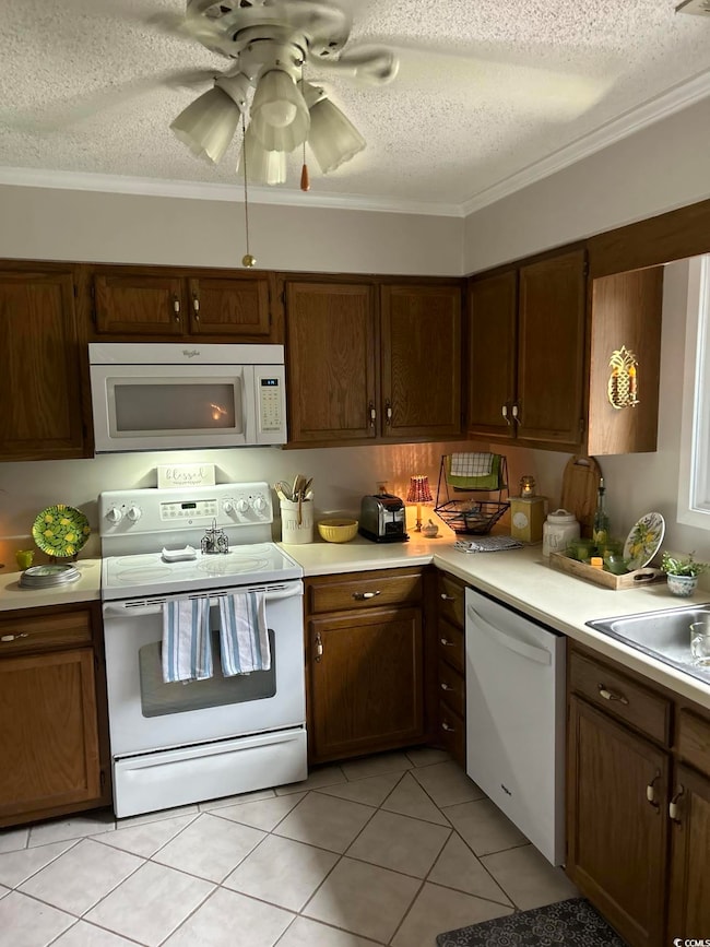 Kitchen with white appliances, a textured ceiling, light countertops, ornamental molding, and light tile patterned flooring