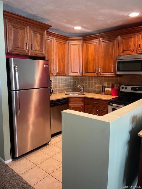 Kitchen with appliances with stainless steel finishes, decorative backsplash, light tile patterned flooring, brown cabinetry, and a peninsula