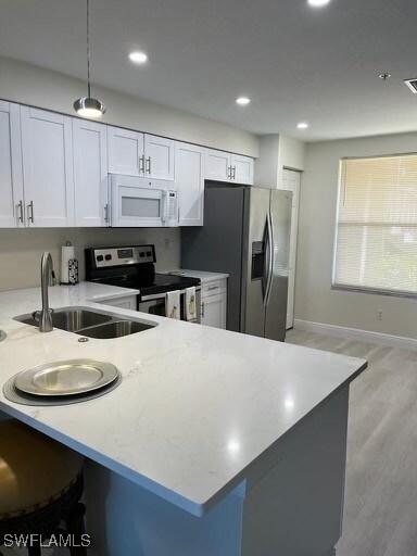 Kitchen with white cabinets, kitchen peninsula, stainless steel appliances, and hanging light fixtures