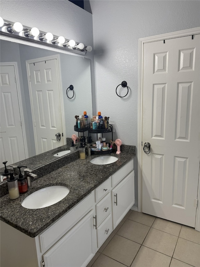 Bathroom featuring double vanity, light tile patterned flooring, and a textured wall