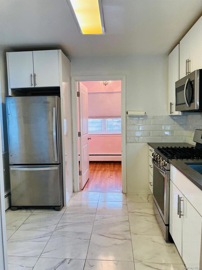 Kitchen featuring white cabinetry, appliances with stainless steel finishes, light marble finish floors, and backsplash