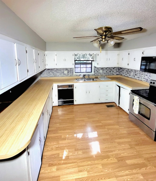 Kitchen featuring black appliances, light wood-style flooring, a sink, a textured ceiling, and decorative backsplash